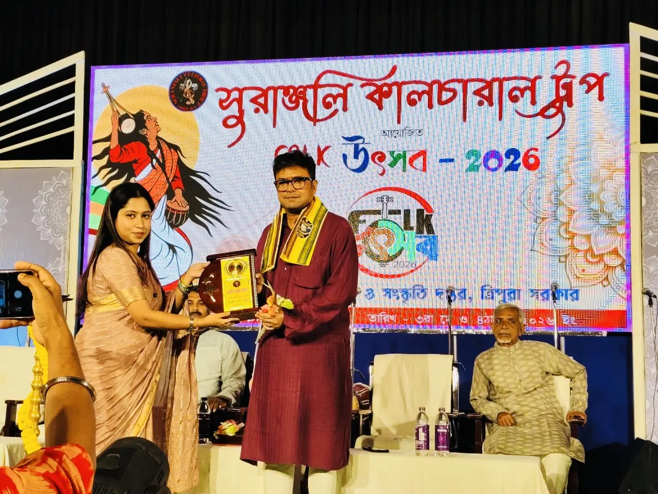 Dr. Jayanta Ghosh of NextChapter Academy being felicitated with a shawl and memento on stage at Folk Utsav 2026, organised by Surangjali Cultural Group in Tripura