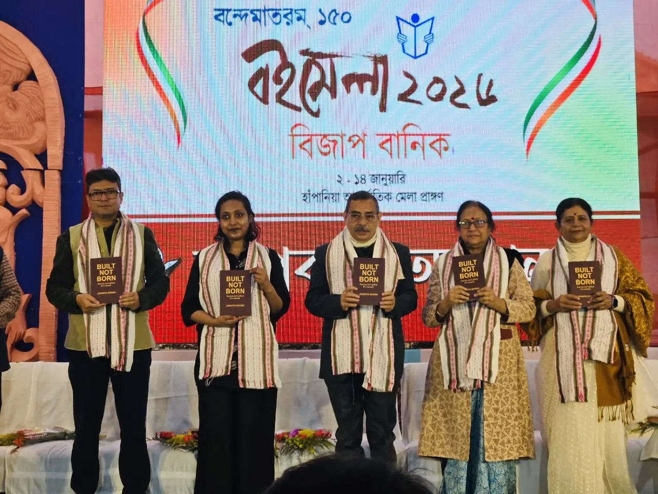 Dignitaries and Dr. Jayanta Ghosh holding up copies of the book Built Not Born during its unveiling at Boi Mela 2026, the Agartala Book Fair